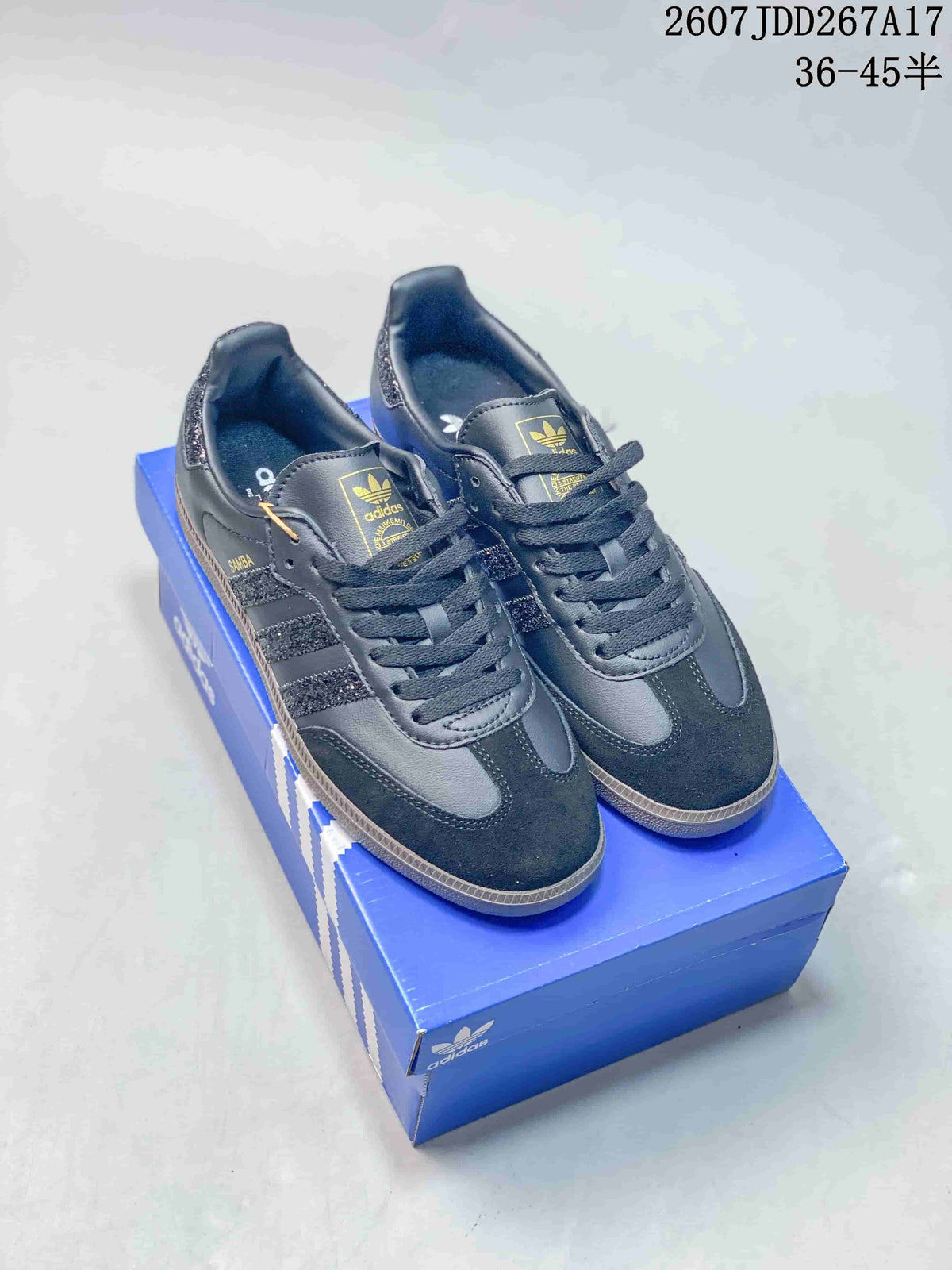 Black adidas Samba sneakers displayed on a blue shoebox, with gold-tone branding and a visible size range marking.