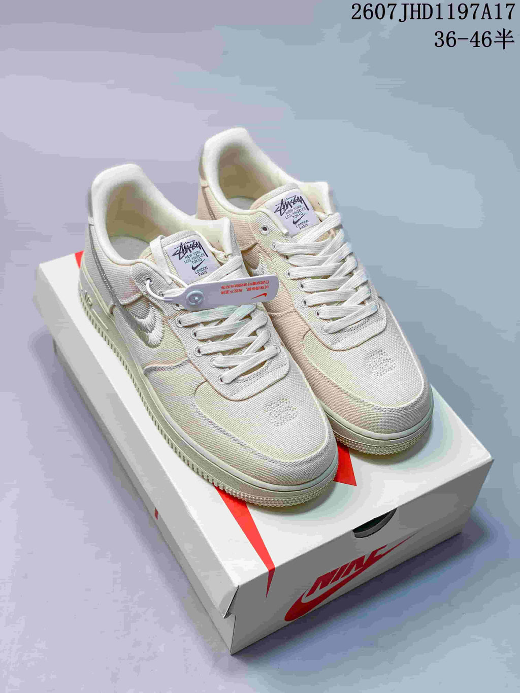 Pair of cream Stussy x Nike Air Force 1 '07 sneakers displayed on a shoebox, with woven uppers, embroidered Swoosh details, and visible product code text.
