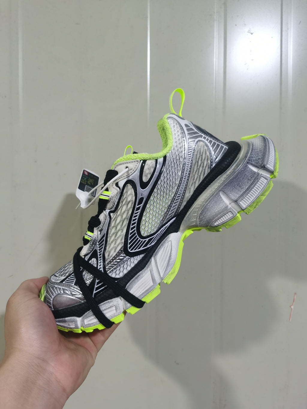 Angled view showing the sneaker’s layered upper, fluorescent-yellow collar and outsole accents, and black laces.
