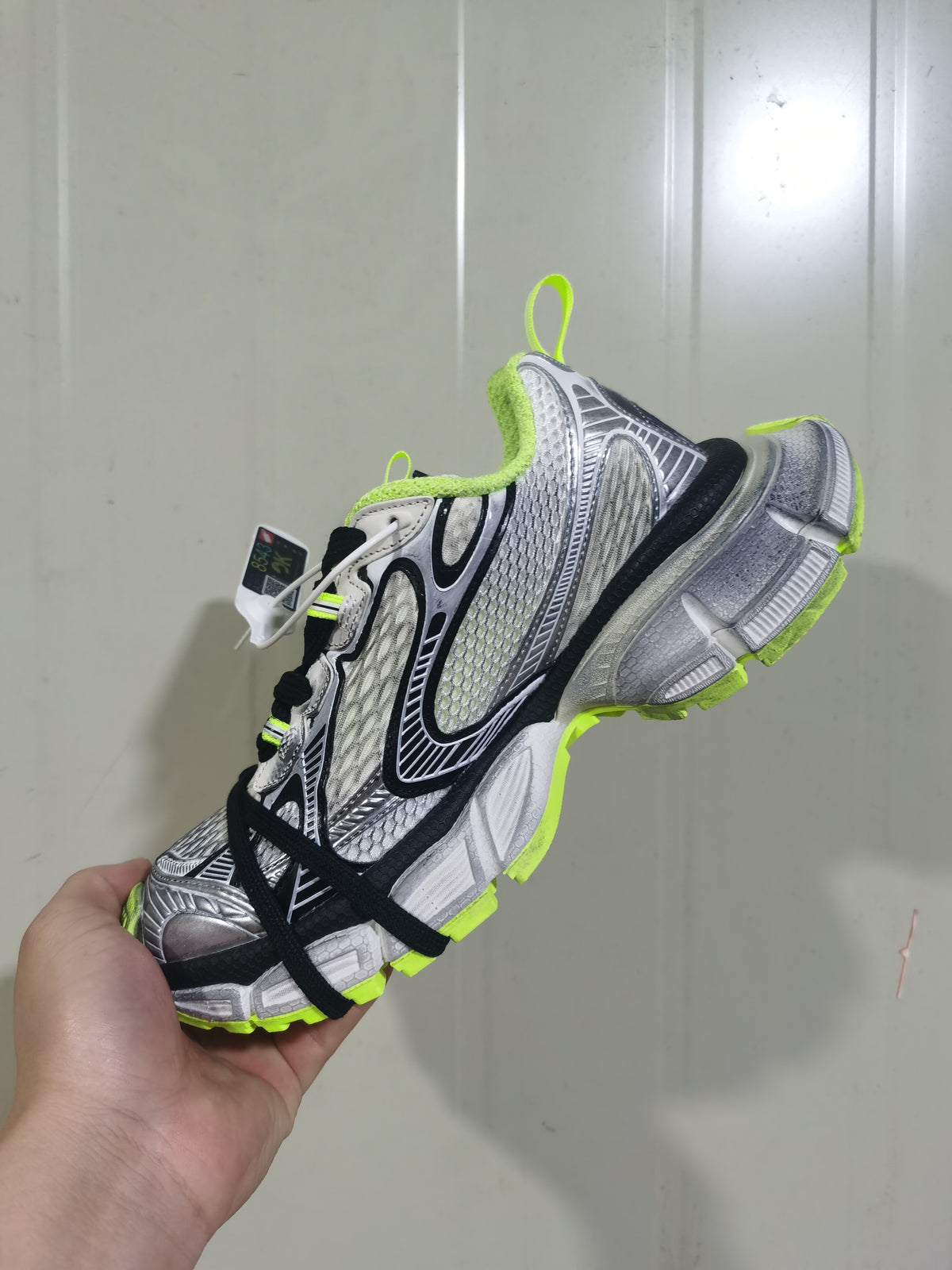 Angled view showing the sneaker’s layered upper, fluorescent-yellow collar and outsole accents, and black laces.