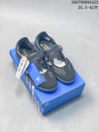 Black adidas Mary Jane-style sneakers displayed on a blue shoebox, showing the strap, mesh panels, and packaging.