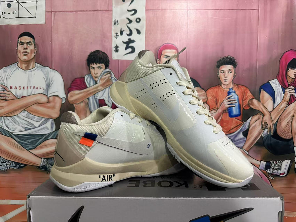 Three-quarter view of paired white Nike basketball sneakers with side swooshes, Kobe-style details and a box visibly marked KOBE.