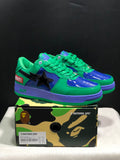 Pair of green, blue and purple Bape Sta low-top sneakers displayed on a camouflage-patterned box; the box label shows EU 42 and 26.5 cm.