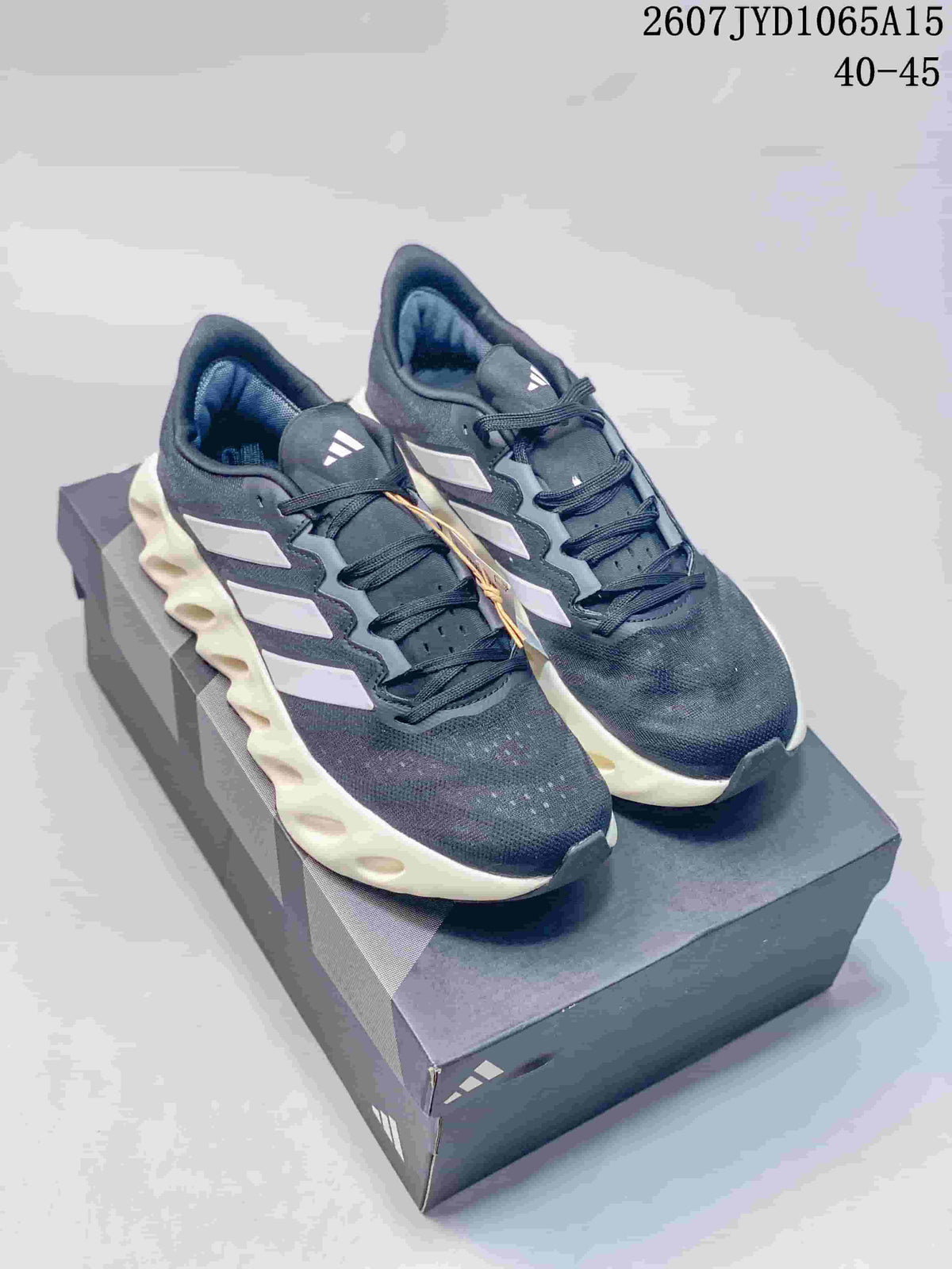 Pair of black and navy Adidas Alphabounce Switch sneakers displayed on a shoebox, with white side details and sculpted light-colored midsoles.