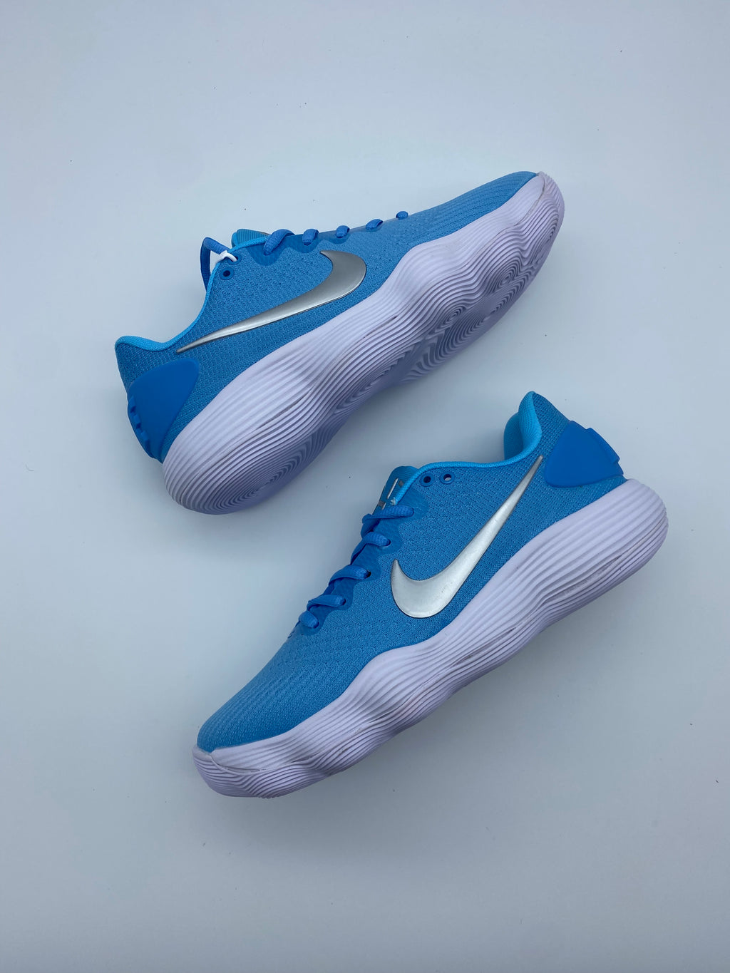 Pair of blue Nike sneakers with silver Swoosh details and ridged white soles, shown from above.