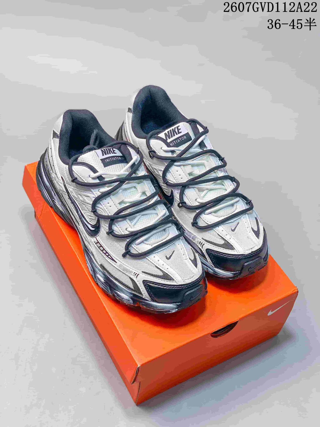 Pair of white and black Nike sneakers displayed on an orange shoebox, showing layered panels and dark laces.