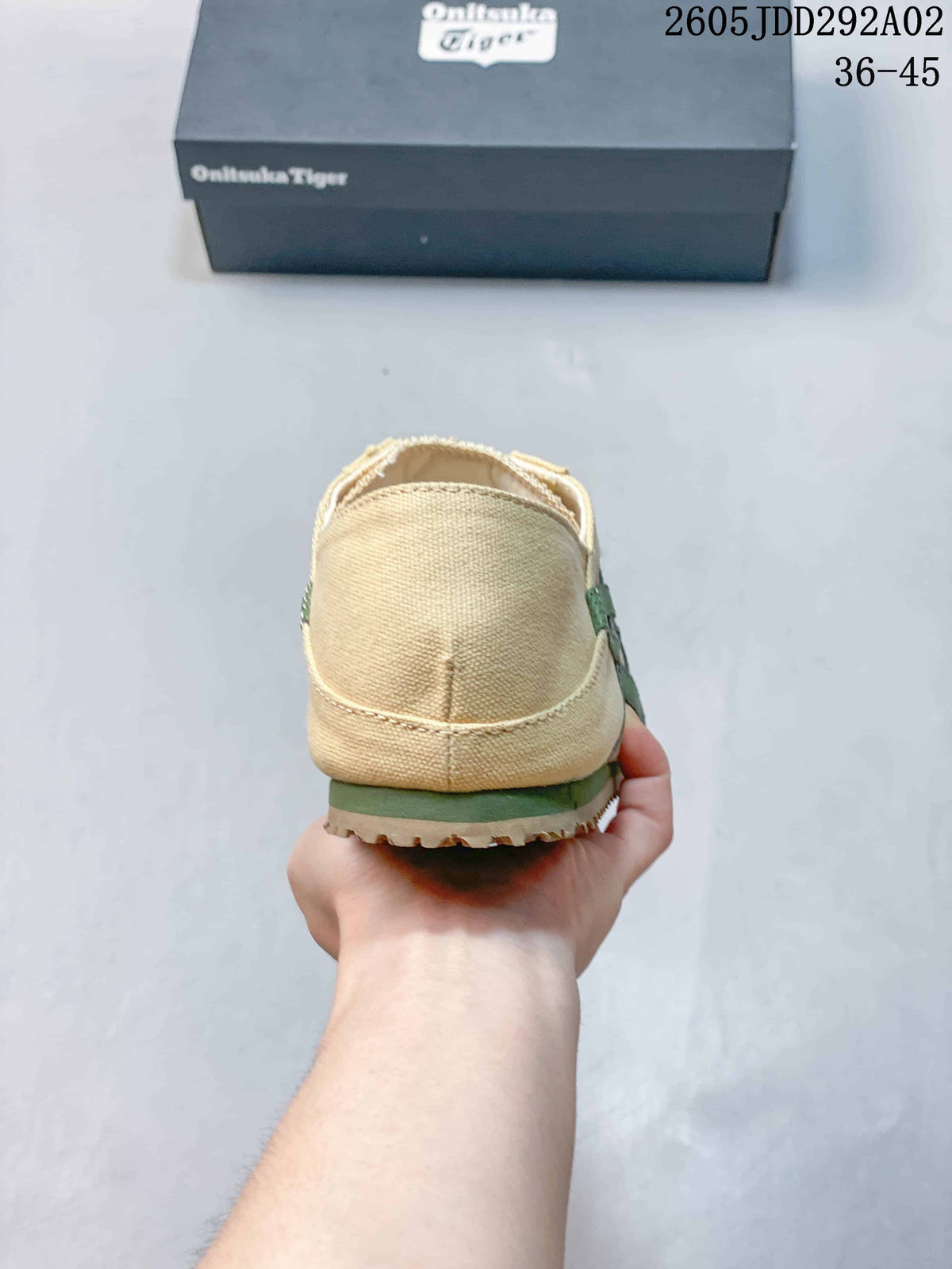 Rear view of the beige slip-on sneaker showing the canvas-like heel panel, green side detail, and textured outsole edge.