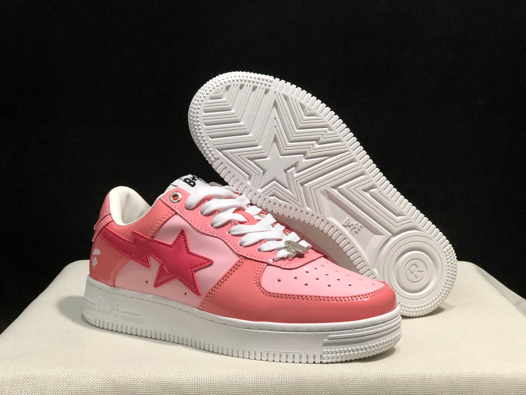 Angled view of the pink BAPE Sta sneakers with one shoe lifted to show the white patterned outsole and central star detail.