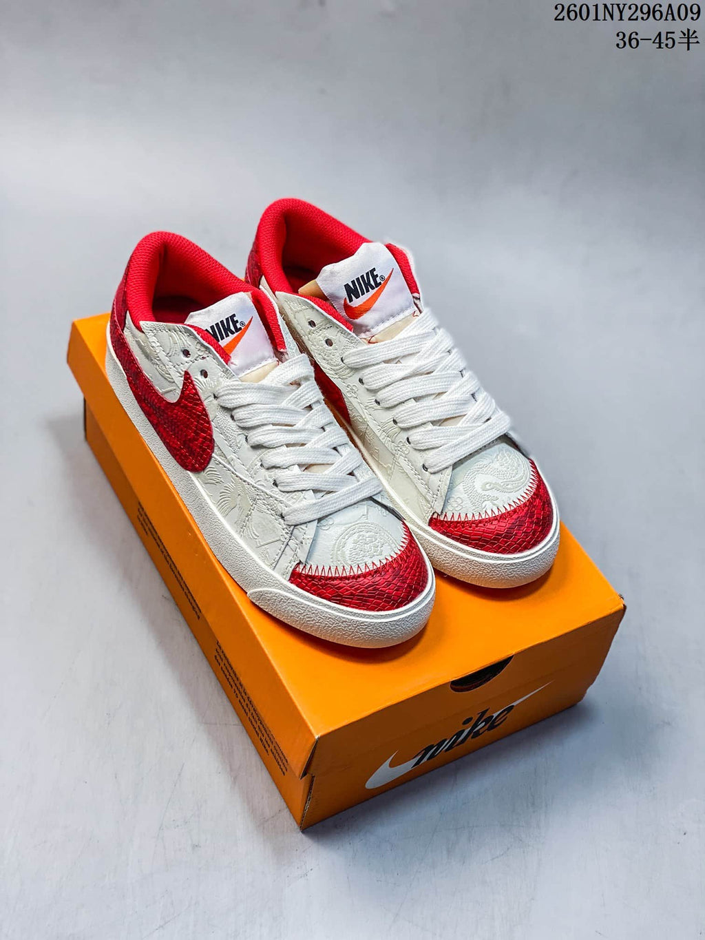 Pair of white and red Nike Blazer Low ’77 Jumbo sneakers displayed on an orange shoebox.