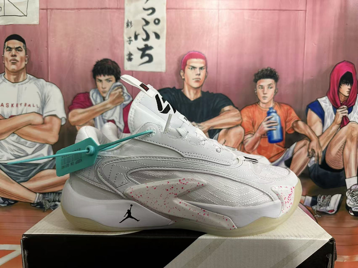 Side view of a white Jordan basketball sneaker showing stitched overlays, red speckled accents and a translucent outsole.