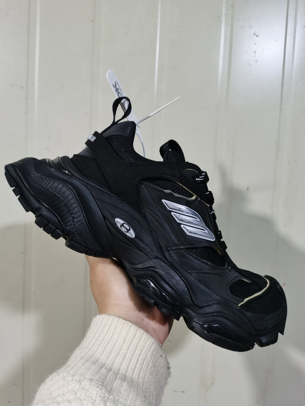Close angled view of the black and white sneaker showing layered panels, mesh sections, metallic side detailing, and a chunky outsole.