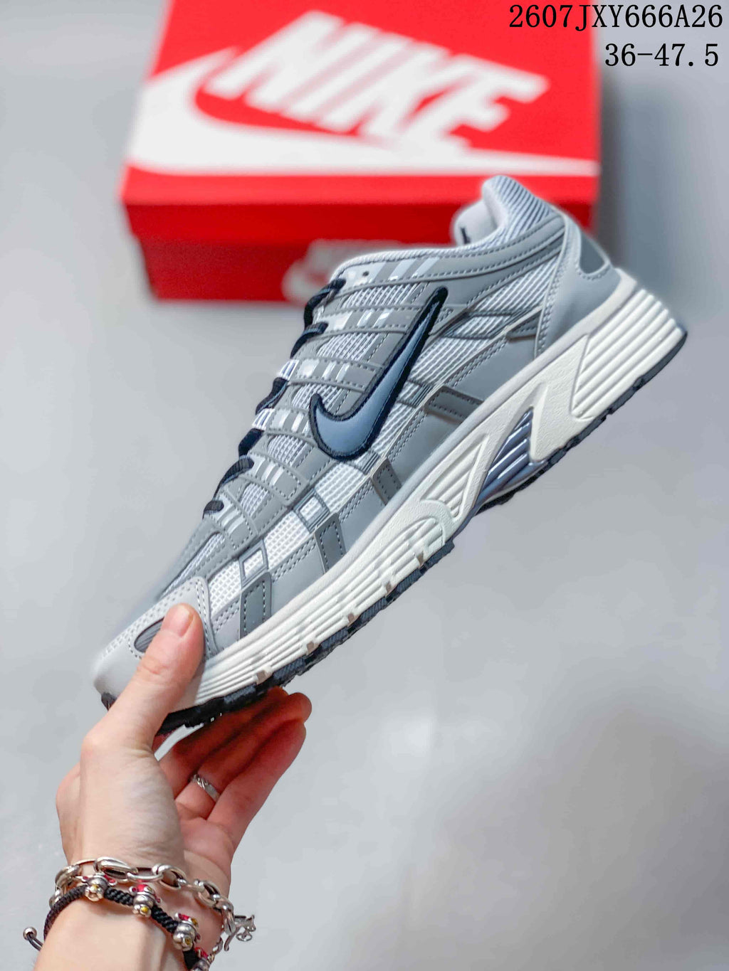 Side profile of a gray and white Nike P-6000 sneaker showing mesh panels, layered overlays, dark Swoosh detailing, and a textured outsole.