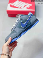 Side view of a grey and blue low-top sneaker showing the contrasting blue side logo, perforated upper panels, and blue outsole.