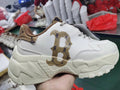 Side view of a white chunky sneaker with beige and khaki patterned accents and a large letter graphic.