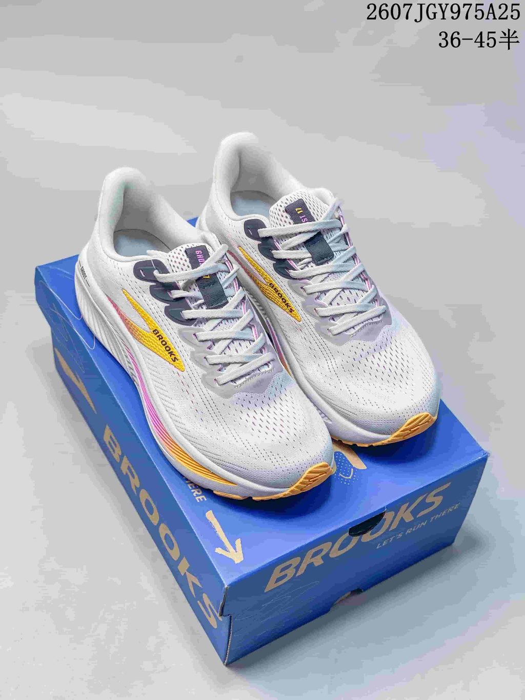 Pair of white Brooks Ghost 17 sneakers with yellow and pink accents displayed on a blue Brooks shoe box.