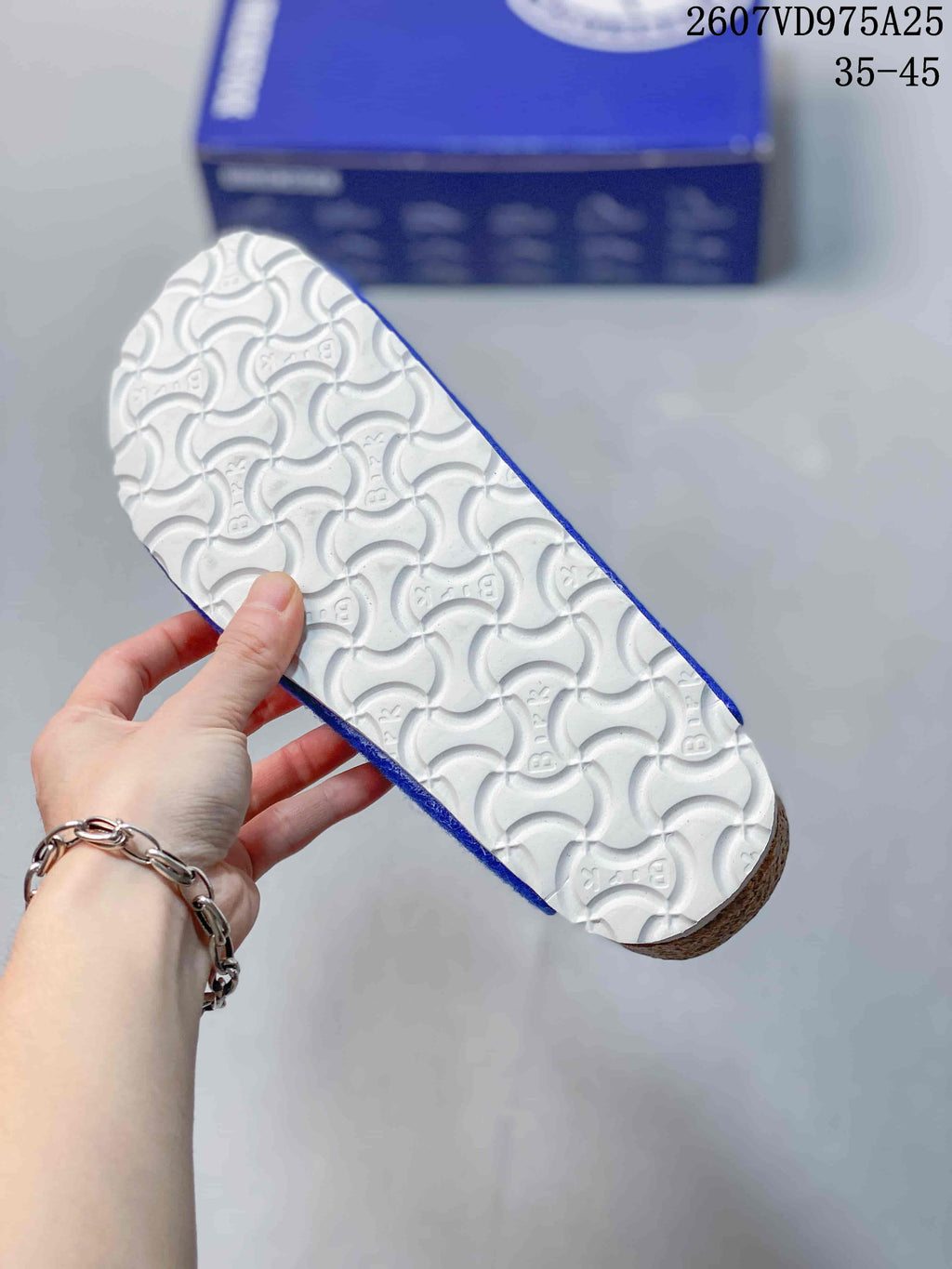Underside of a blue clog showing the white repeating-pattern outsole and cork-colored edge.