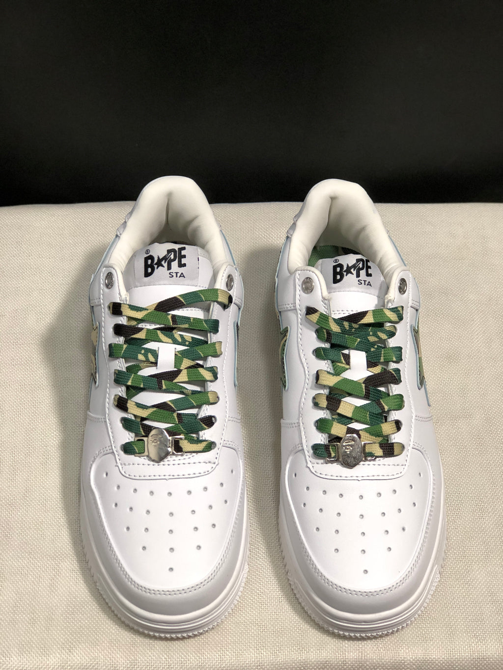 Front top view showing the white perforated toe boxes and green camouflage laces with metal lace accents.