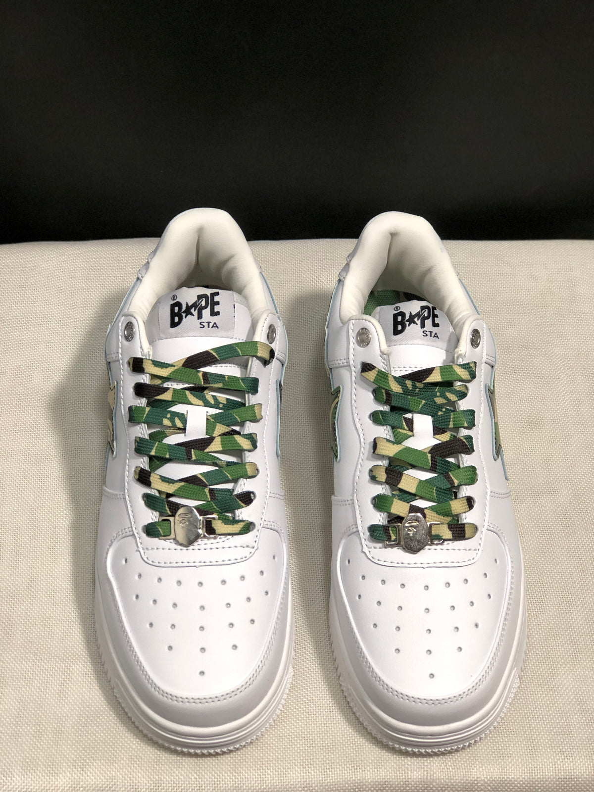 Front top view showing the white perforated toe boxes and green camouflage laces with metal lace accents.