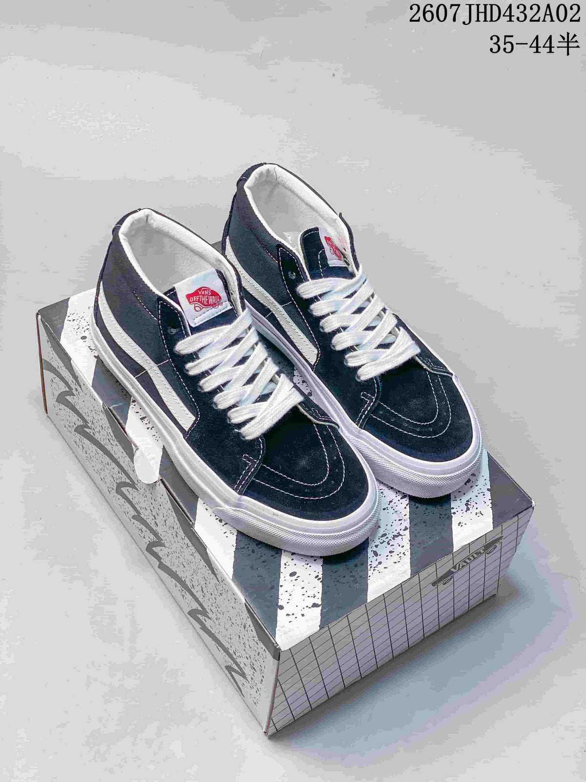 Pair of black-and-white Vans mid-top sneakers displayed on a patterned box