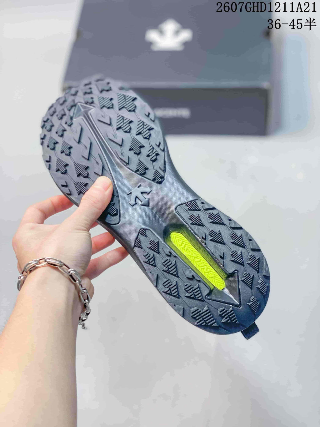 Underside view of a black sneaker showing the lugged outsole with directional tread blocks and a contrasting lime-green insert.