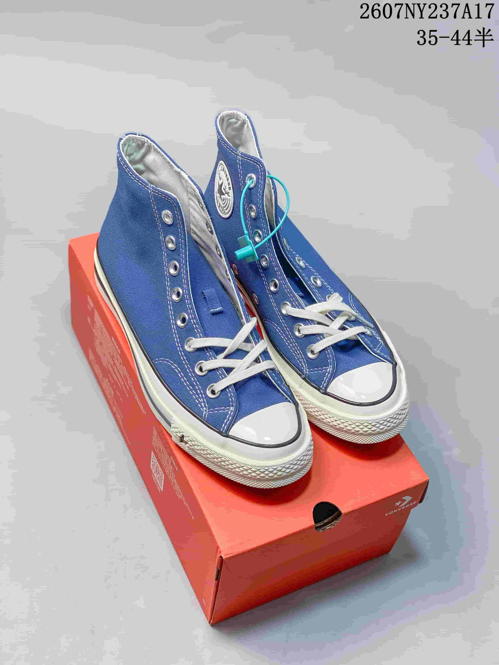 Blue Converse high-top sneakers displayed on a red shoebox, showing the white toe caps, laces, and side patches.