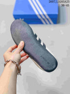 Close-up of the dark textured outsole of a white adidas sneaker, with adidas branding molded near the heel.