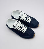 Top three-quarter view of a pair of deep blue sneakers with white laces and visible Alo branding on the tongues.