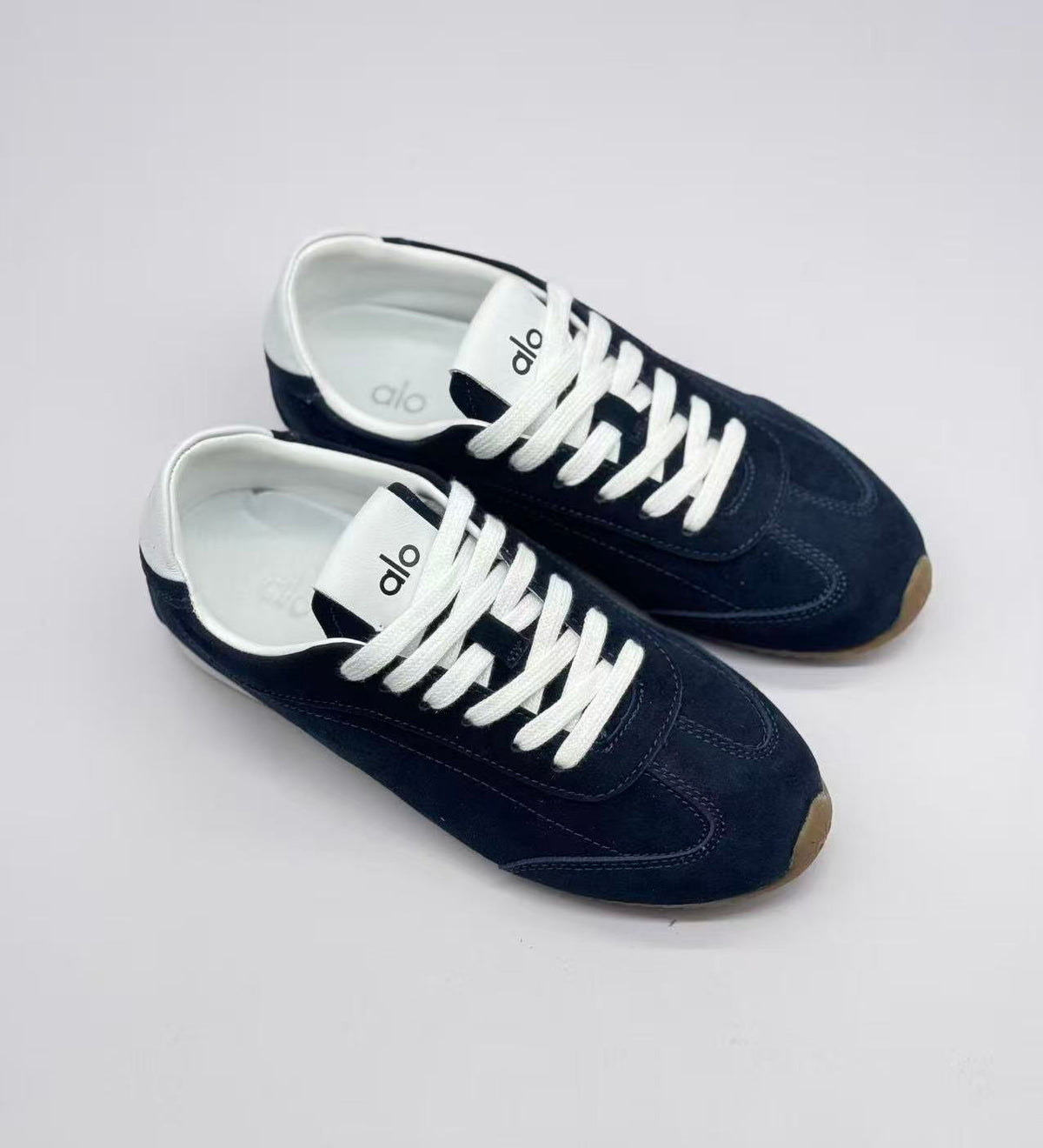 Top three-quarter view of a pair of deep blue sneakers with white laces and visible Alo branding on the tongues.