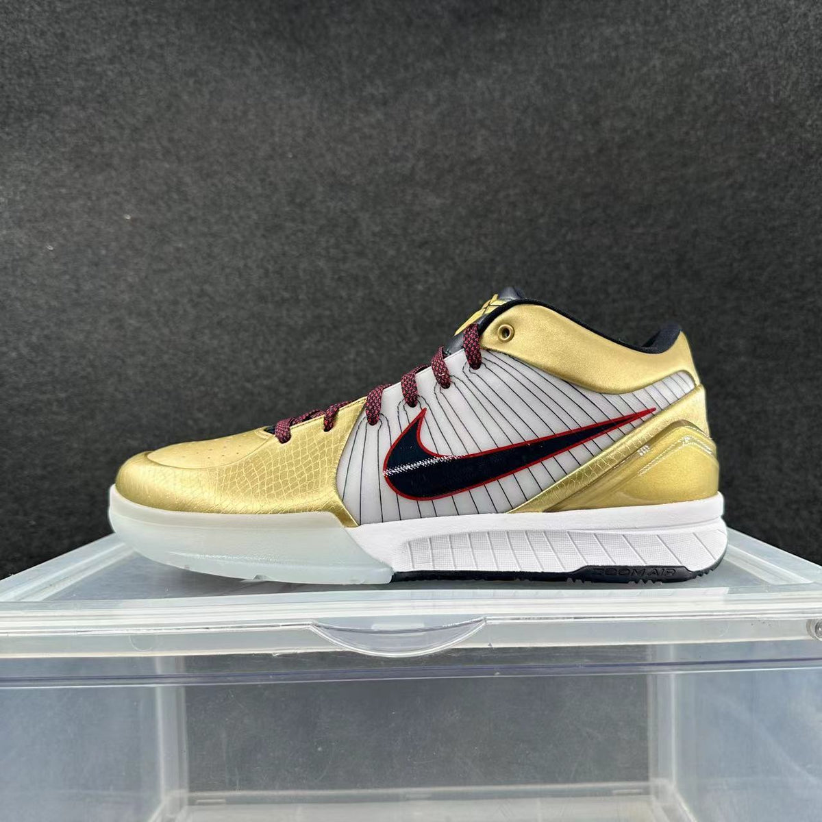 Side view of a gold, white, and dark red low-top basketball shoe with pinstriped panels and a dark side logo.
