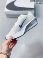 Side view of a white Nike running shoe with a dark navy Swoosh, sculpted midsole, and visible ZoomX branding.