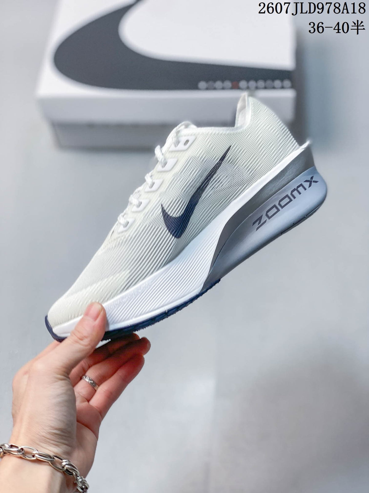 Side view of a white Nike running shoe with a dark navy Swoosh, sculpted midsole, and visible ZoomX branding.