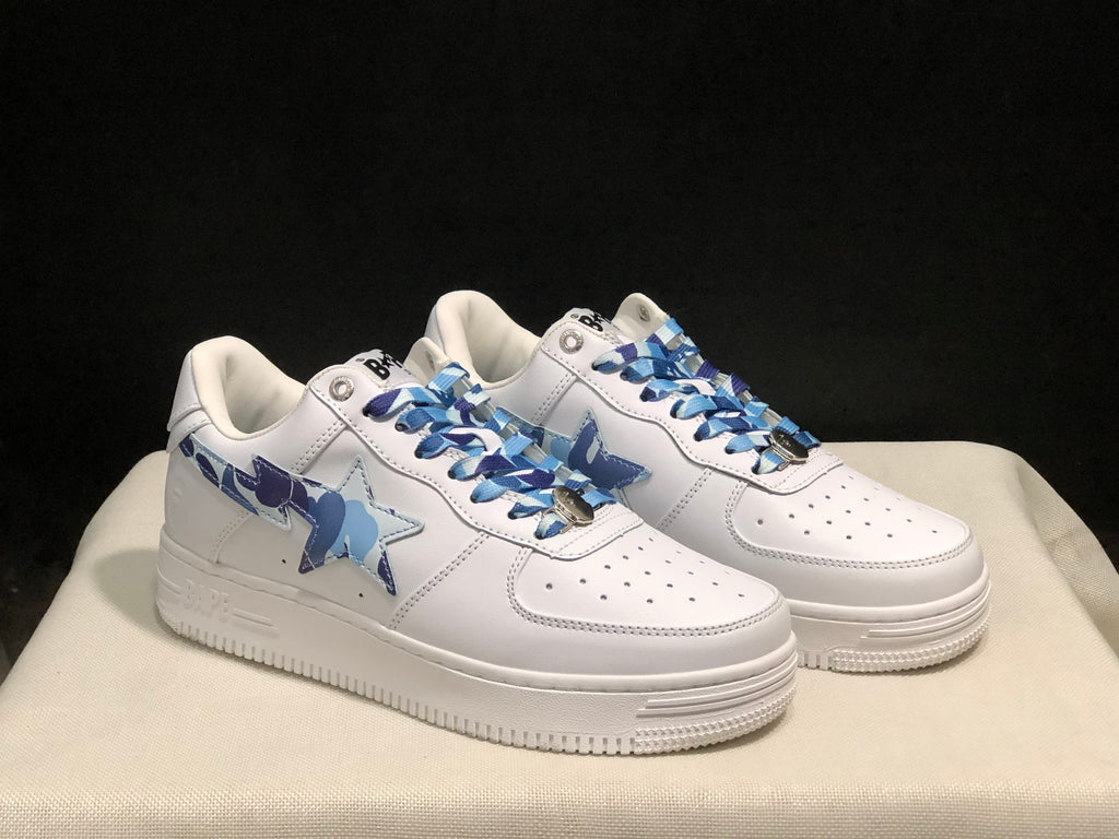 Three-quarter front view of the white BAPE STA sneakers with blue camouflage side detailing.