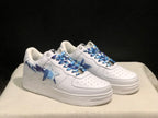 Three-quarter front view of the white BAPE STA sneakers with blue camouflage side detailing.