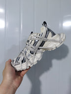 Side view of the white and black sneaker showing the layered lace structure, padded collar, and segmented outsole.