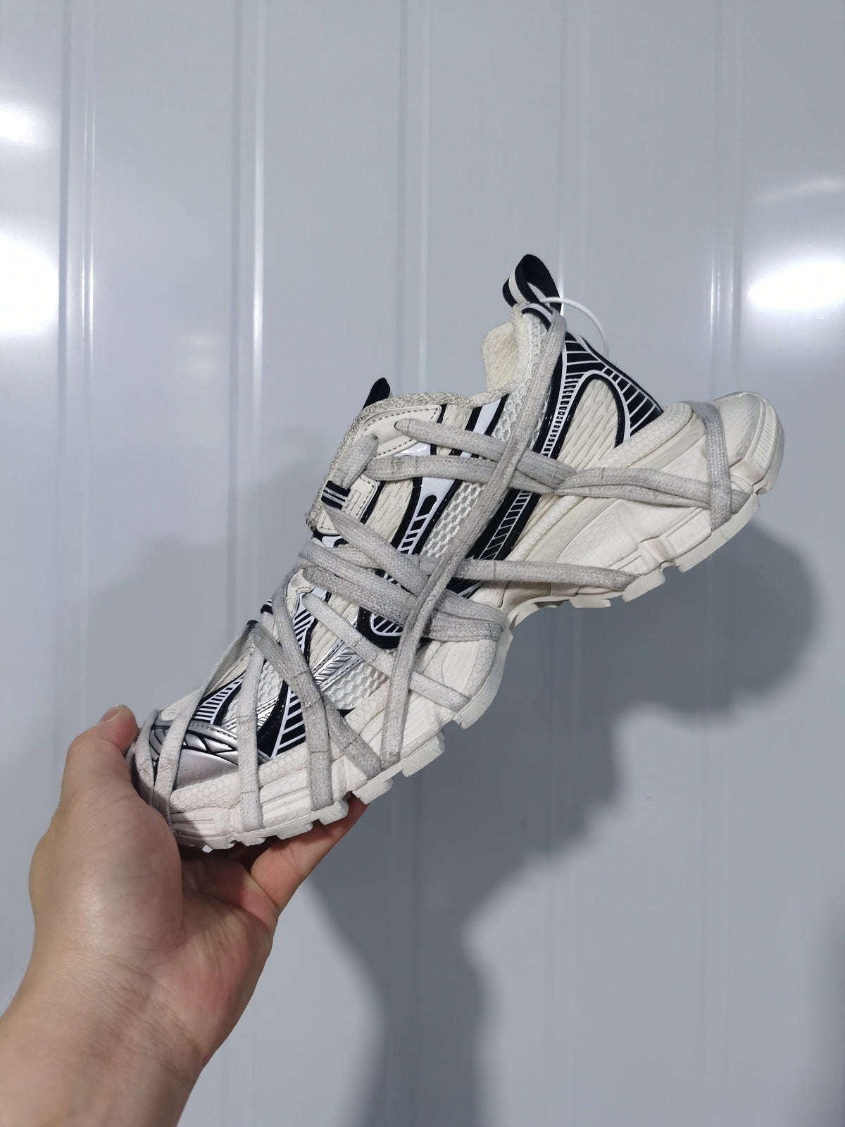Side view of the white and black sneaker showing the layered lace structure, padded collar, and segmented outsole.