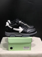 Side view of black low-top sneakers with white arrow details, white heel accents, gray midsoles, and black outsoles.