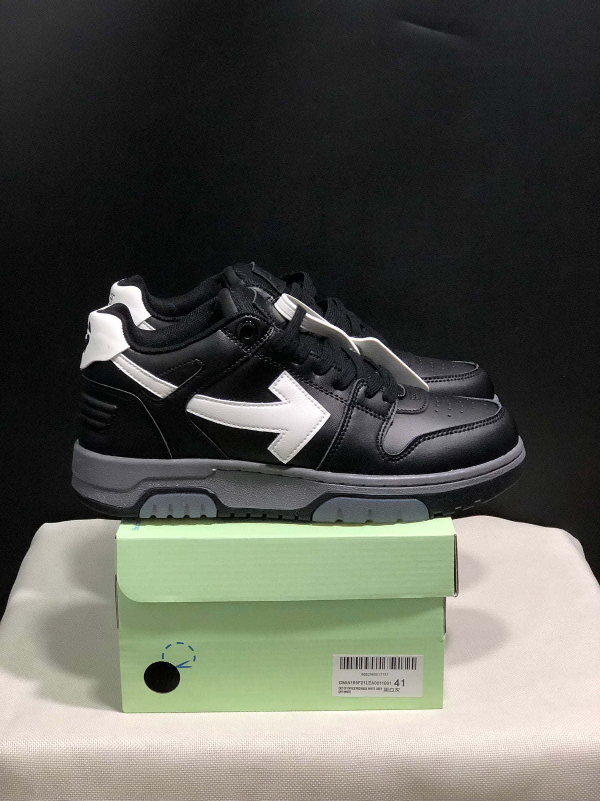 Side view of black low-top sneakers with white arrow details, white heel accents, gray midsoles, and black outsoles.
