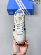 Top view of the sneaker showing white laces, a white textured upper, and gold-toned adidas tongue branding.