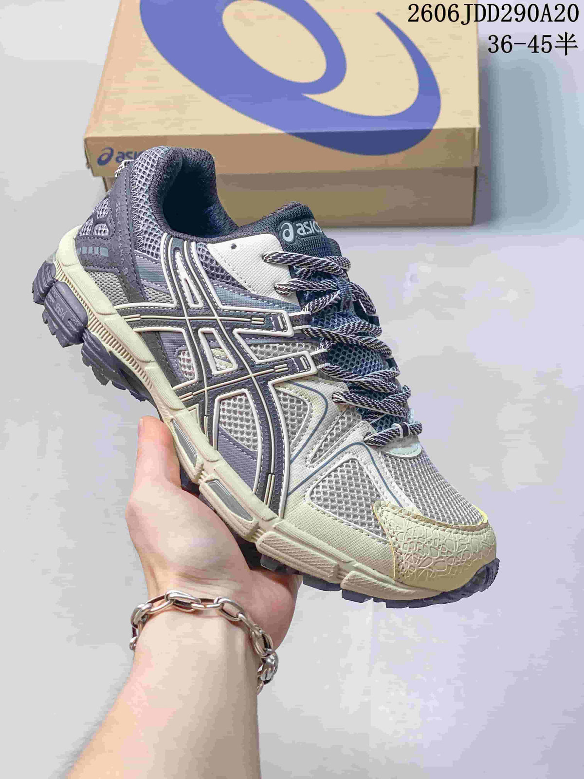 Grey and cream ASICS Gel-Kahana 8 sneaker held in front of a shoebox