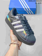 Angled view of the black Superstar sneaker with white stripes and multicolor splatter accents.