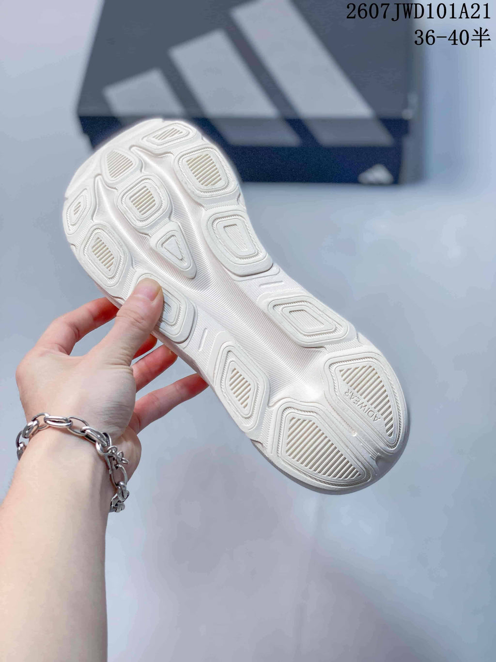 Close view of the white patterned outsole, showing multiple raised traction sections and the Adidas shoebox in the background.