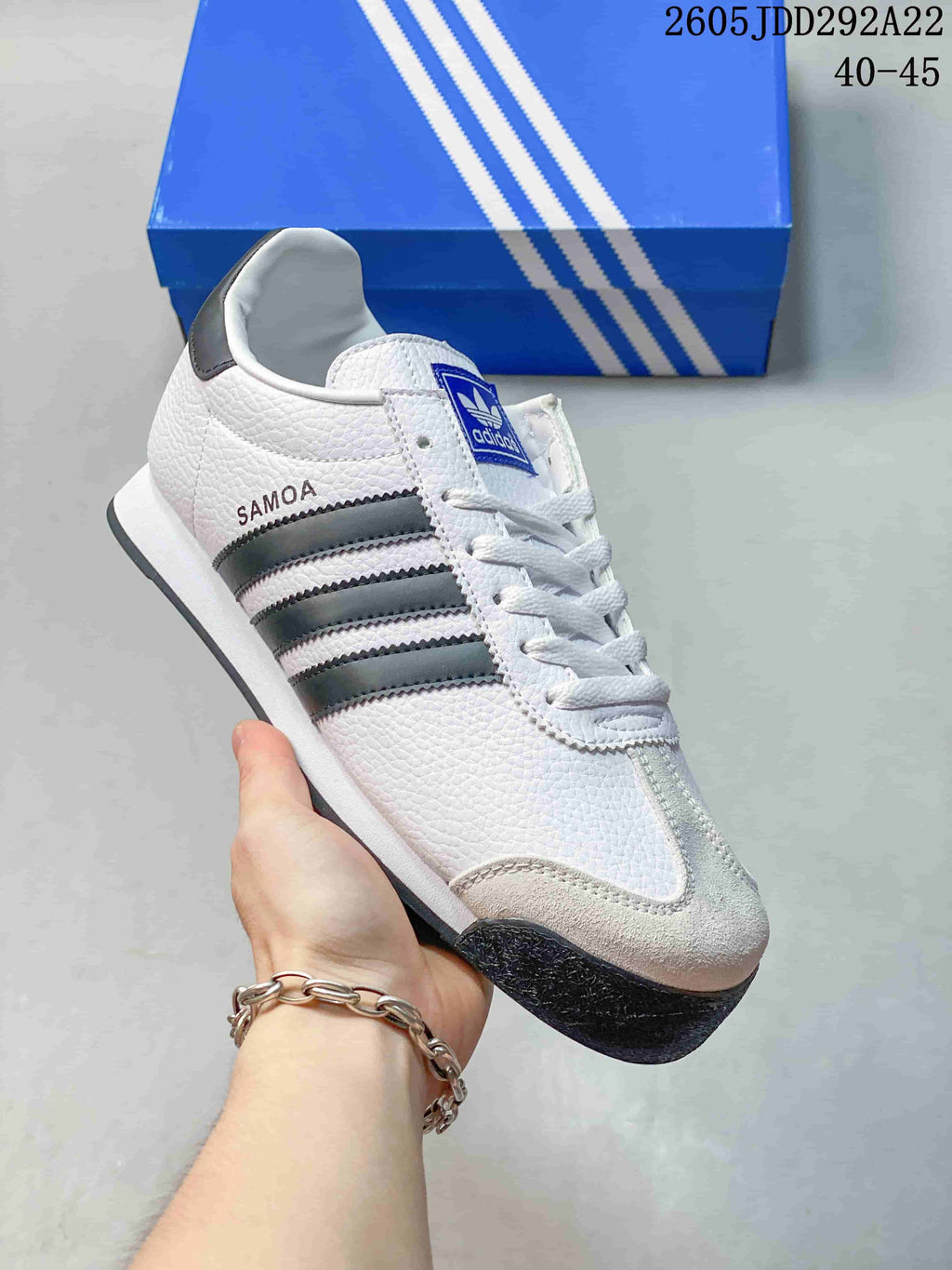 Angled side view of the white and black sneaker showing SAMOA side branding, three stripes, and the dark outsole.