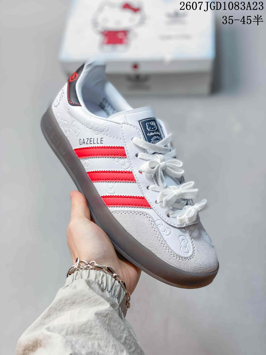 Angled side view showing the white upper, red stripes, Gazelle side branding, Hello Kitty graphics, and dark outsole.
