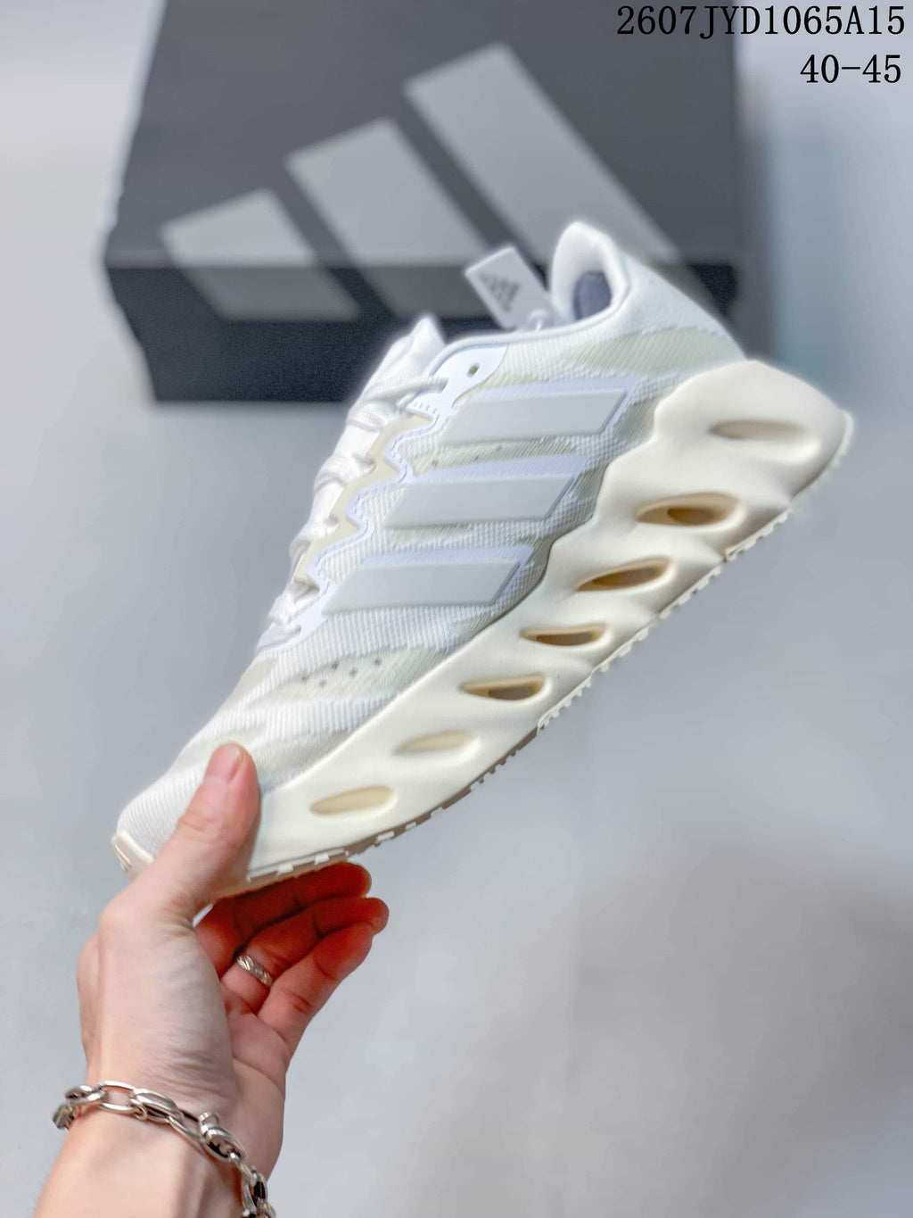 Side profile of the white Adidas sneaker showing layered side stripes, textured upper, and sculpted cream-colored midsole.