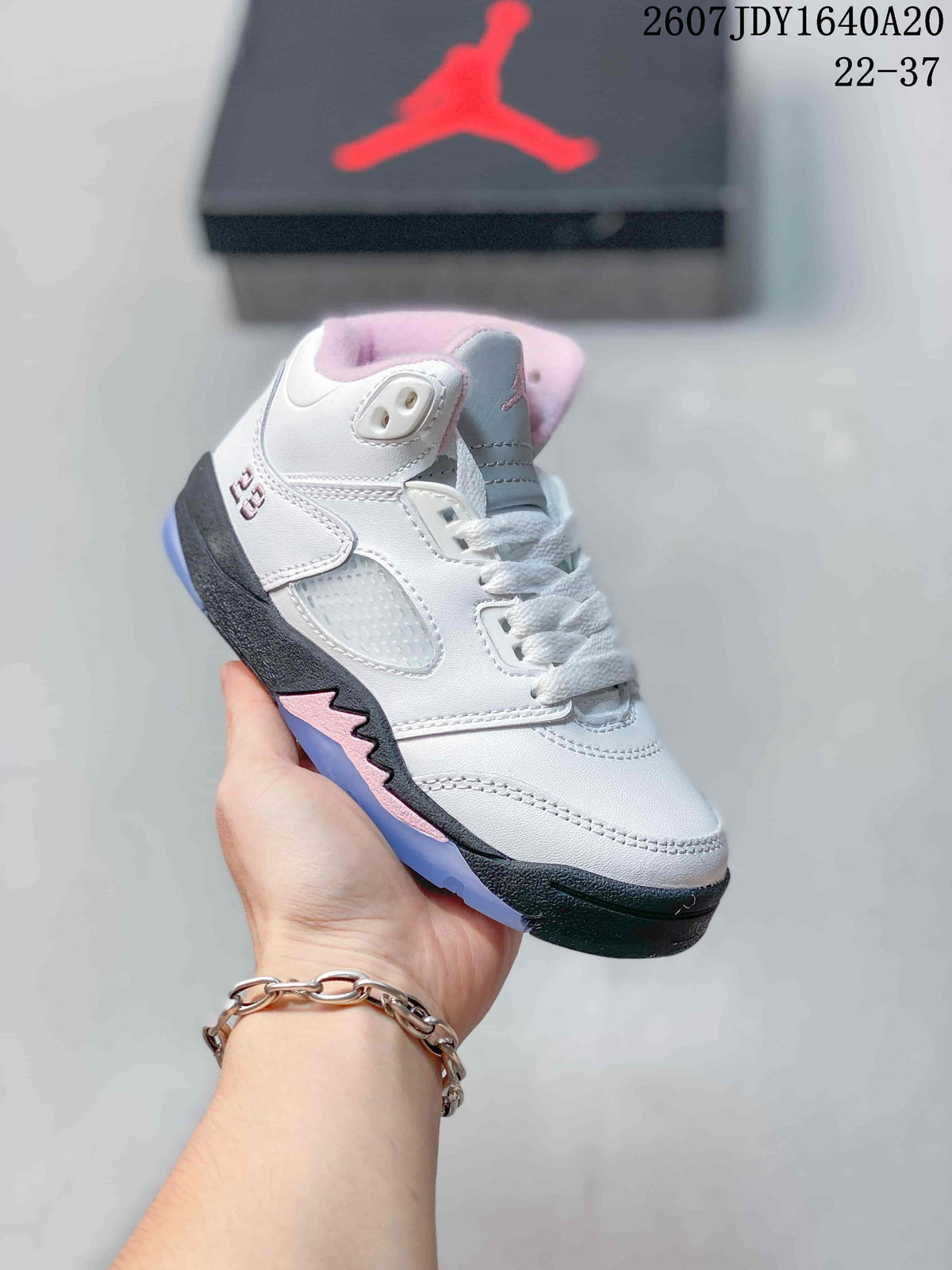 Three-quarter side view of the white mid-top sneaker with pink accents, black midsole, and translucent outsole.