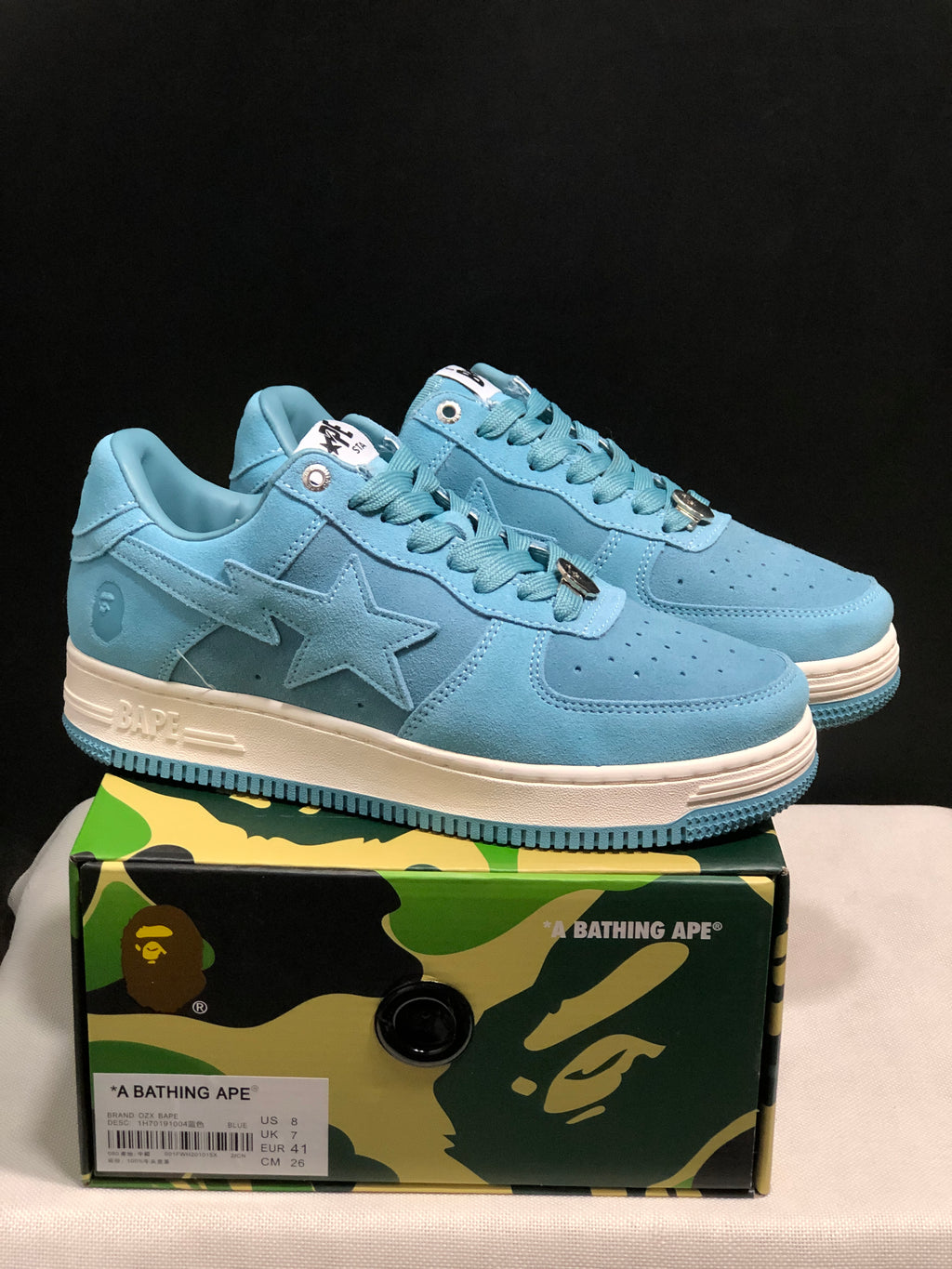Pair of light blue BAPE STA low-top sneakers displayed on a camouflage-branded shoebox; the box label visibly shows US 8, UK 7, EU 41, and CM 26.