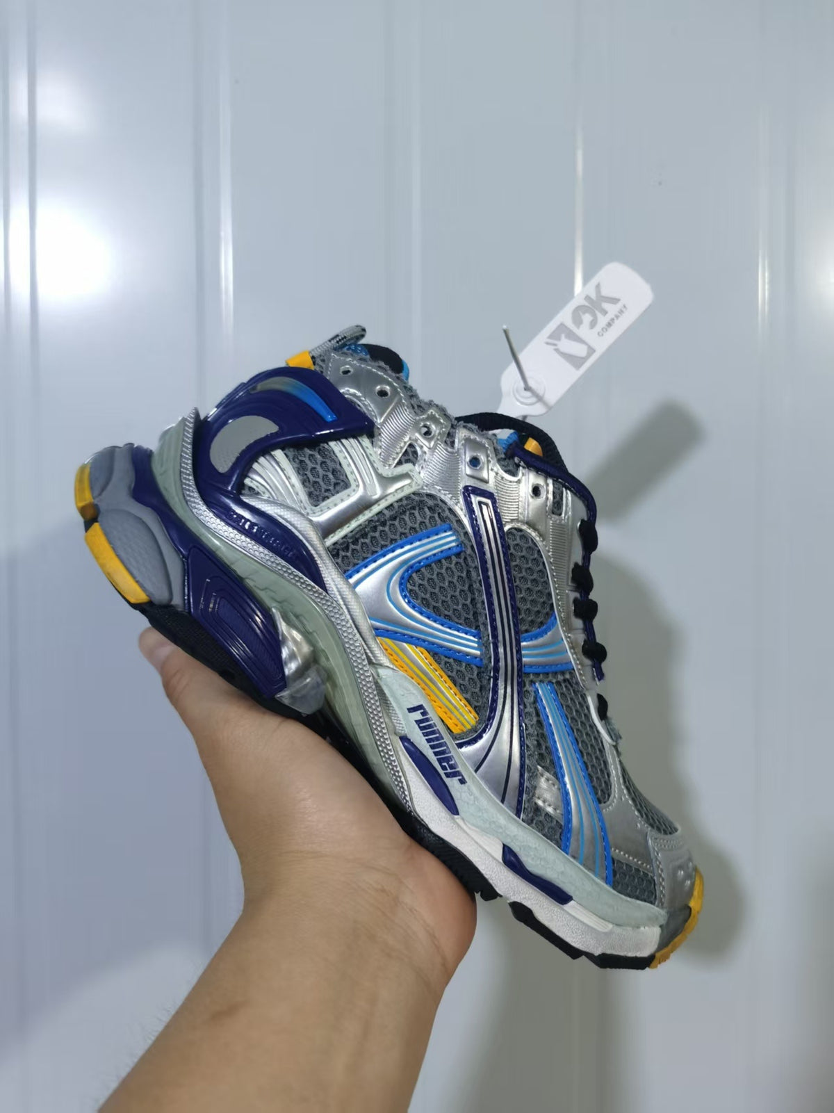 Side and heel view of the grey and blue runner sneaker showing mesh panels, layered overlays and orange outsole accents.