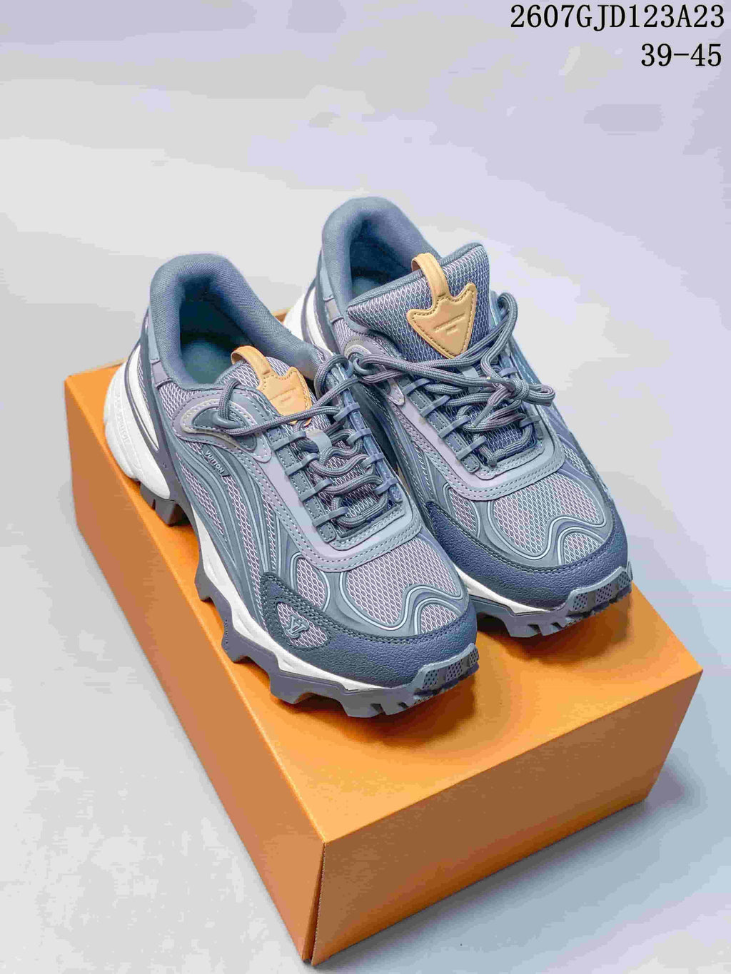 Pair of gray-blue Louis Vuitton Summit sneakers with contrasting gold tongue details displayed on an orange shoe box.
