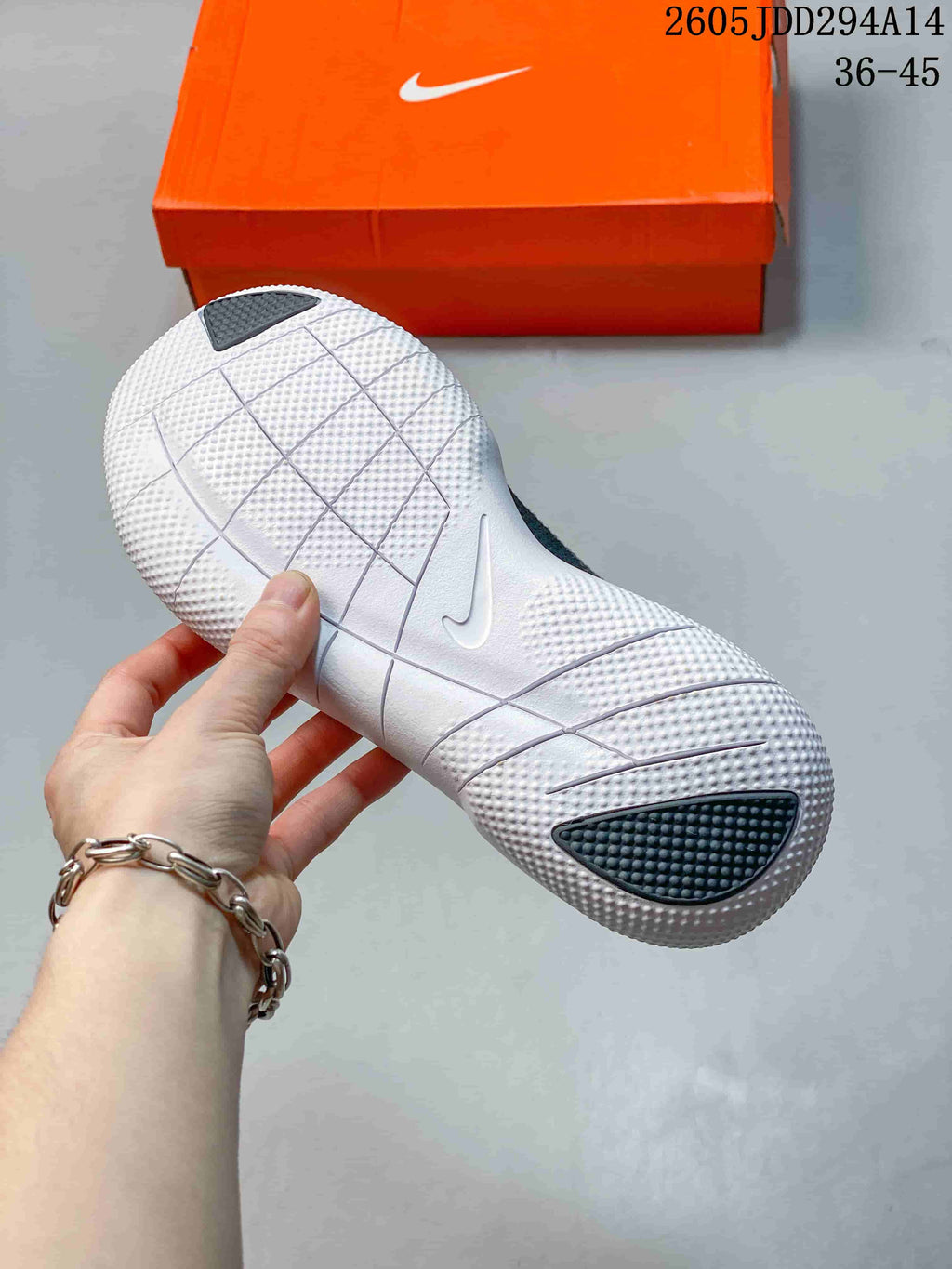 Close-up of the white textured outsole with segmented grooves and dark traction areas, with an orange Nike shoebox in the background.
