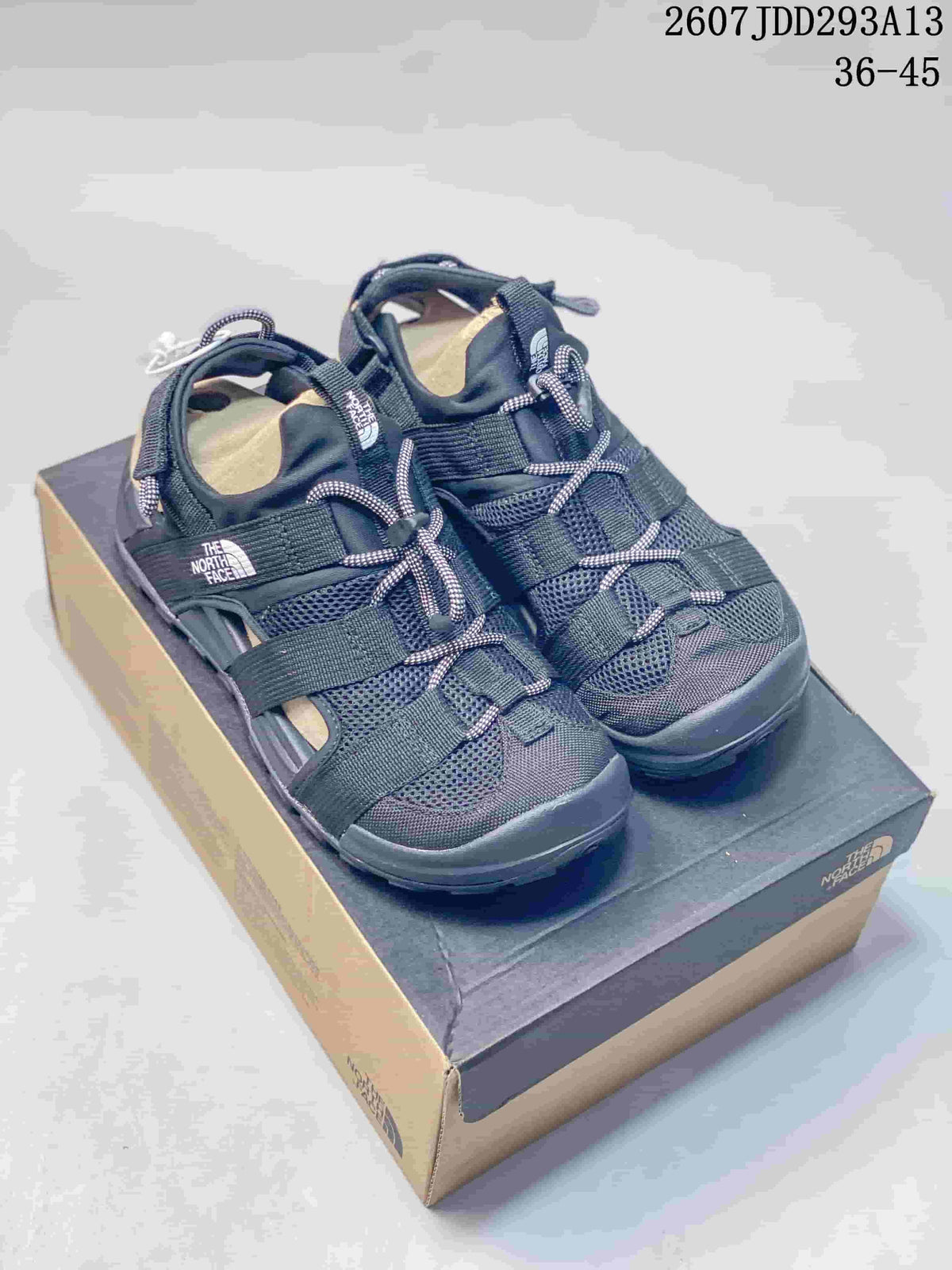 Pair of black The North Face outdoor sandals displayed on a shoebox, showing the strappy upper and front toggle laces.